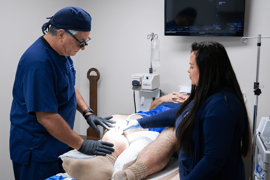 Two doctors perform a varicose vein treatment procedure on a patient's leg