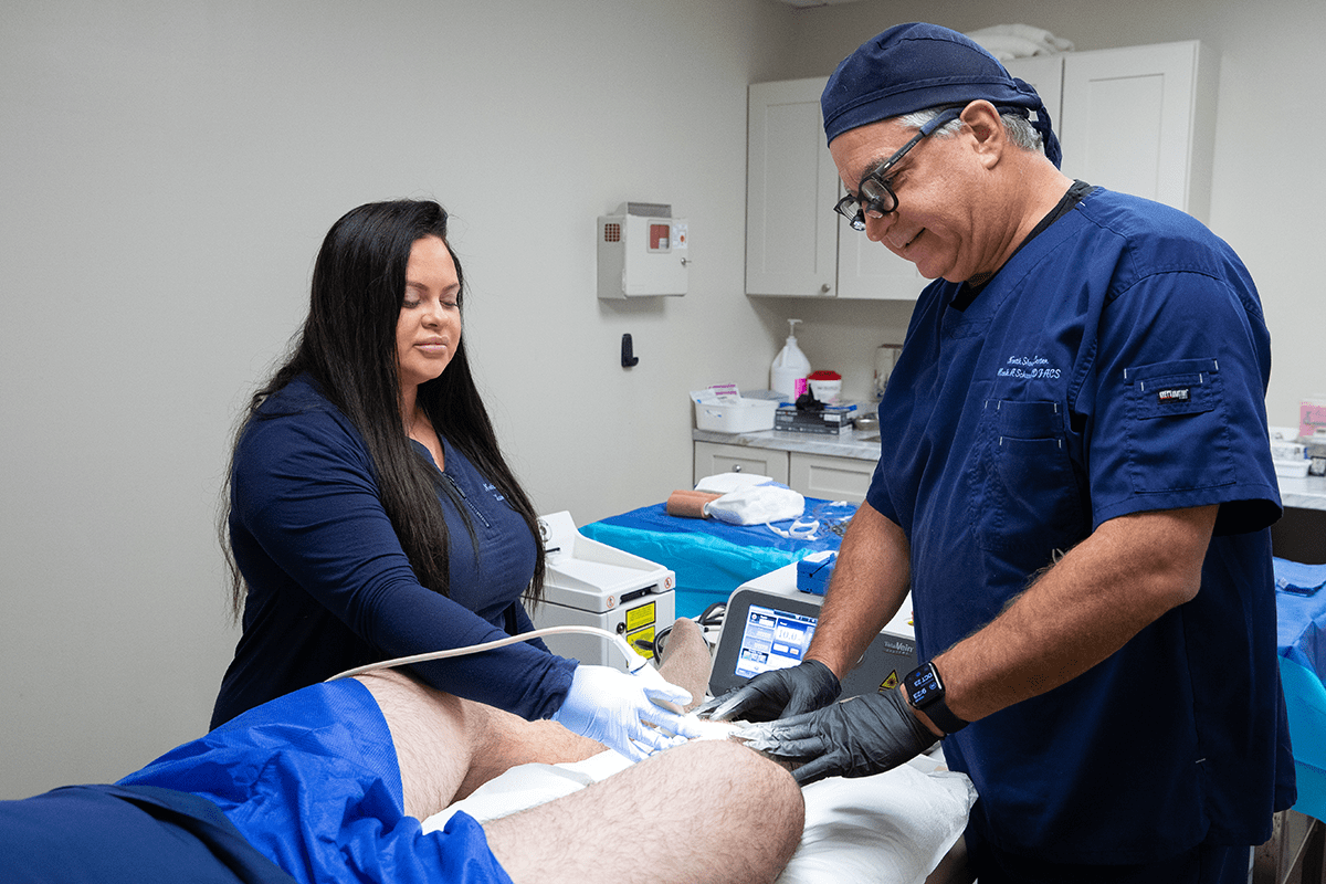 A male doctor and female assistant performing Endovenous Radiofrequency Ablation on a patient's leg