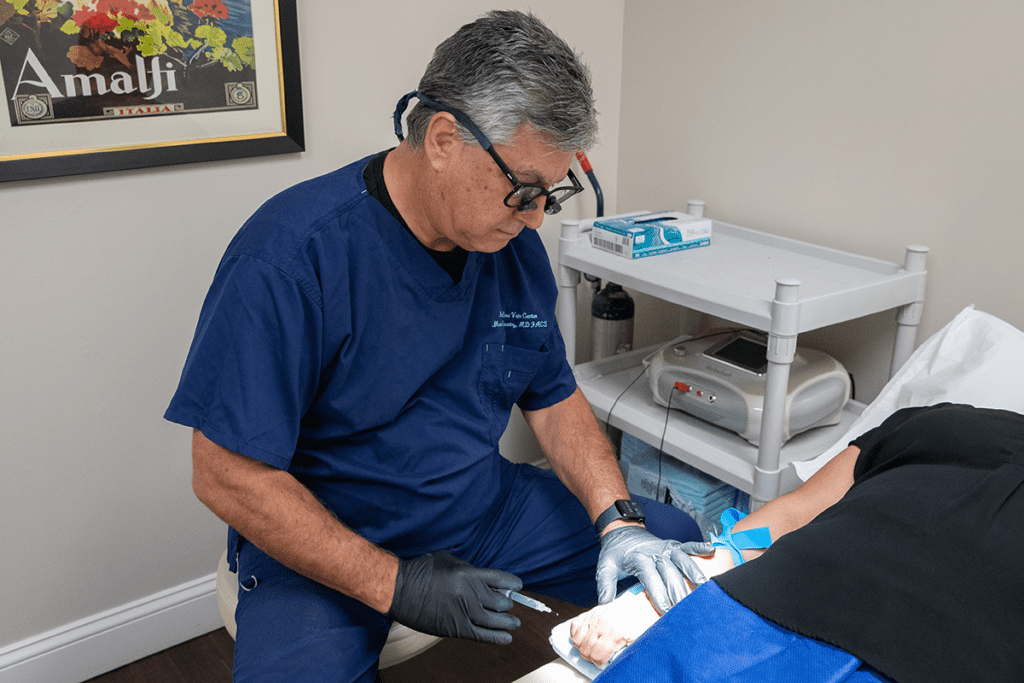 Doctor performing sclerotherapy, a hand vein treatment, on a patient.